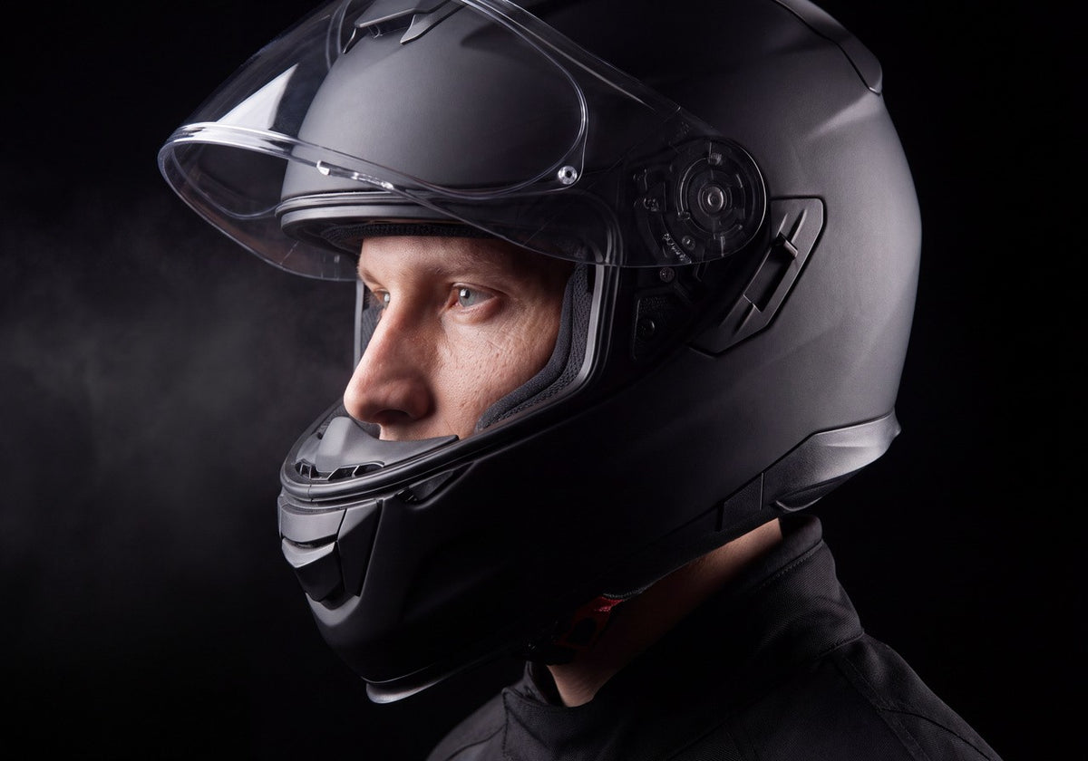 Rider in profile wearing a matte black modular helmet with the visor raised