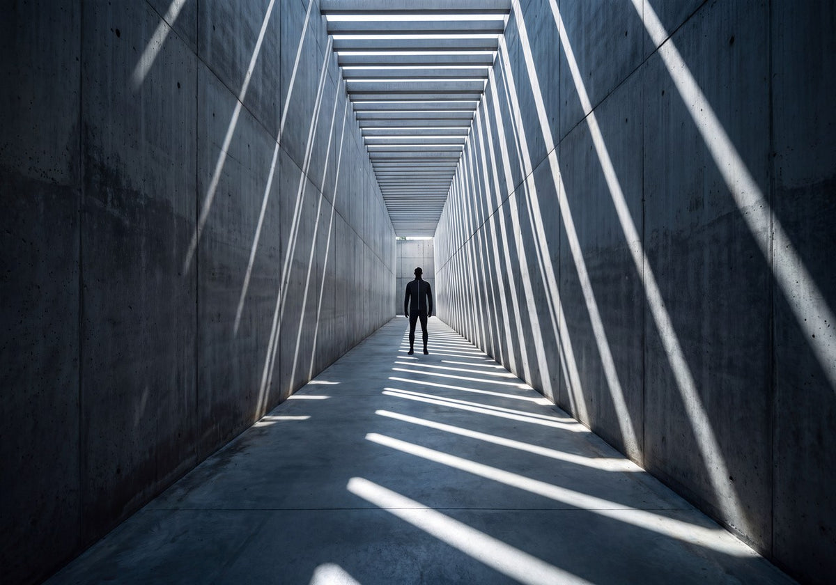 Silhouette at the end of a concrete corridor striped with sunlight
