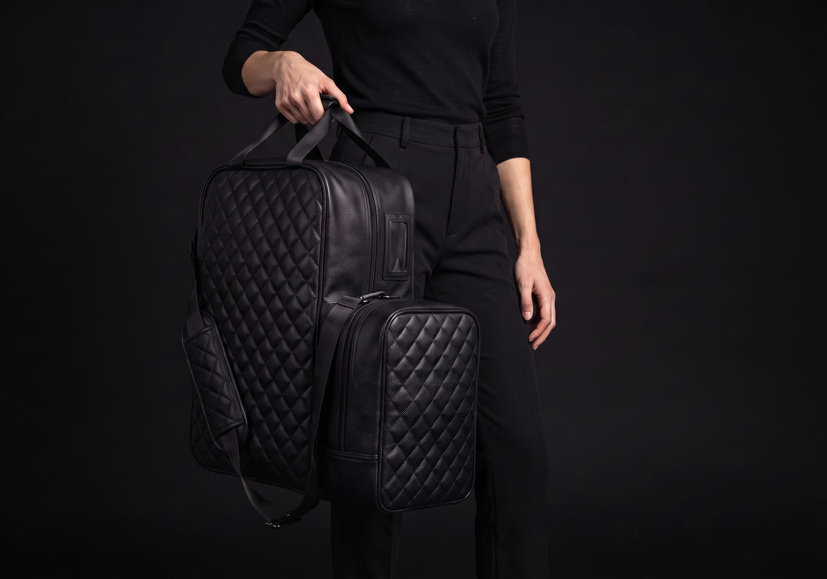 Velmurax quilted boot and helmet bag in black, held by the top handles, strap hanging