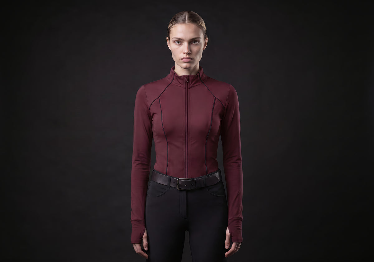 Velmurax women's long-sleeve riding top in burgundy, worn by the model in a front view on the dark studio set